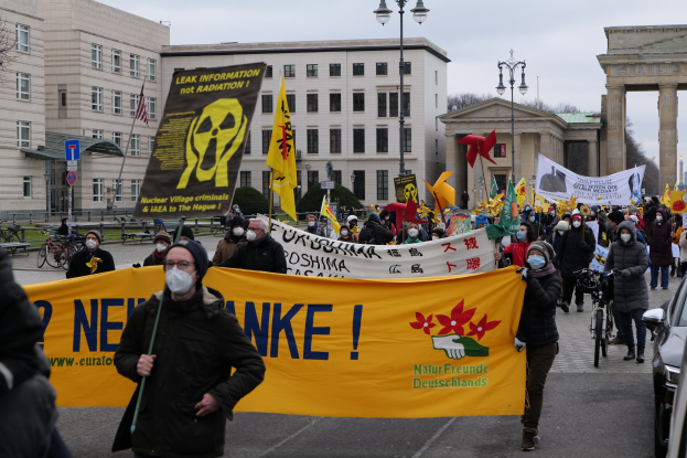 Große Gruppe von Menschen bei einer Straßen-demo gegen Atomkraft in Deutschland, mit Schildern und Fahnen, mit Fahrzeugen und Gebäuden im Hintergrund.