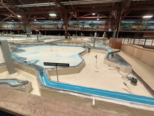 Ein großes Indoor-Wasserpark mit zahlreichen Wasserrutschen, Pfählen, Texttafeln, Deckenleuchten und Wandgemälden, das als Minigolfplatz konzipiert ist, um einen spaßigen und aufregenden Erlebnis zu bieten.