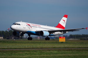 Ein Airbus A320-200 der Austrian Airlines startet vom Frankfurter Flughafen mit einer Tafel im Vordergrund, Gras, Bäumen, Gebäuden und einem klaren blauen Himmel im Hintergrund.