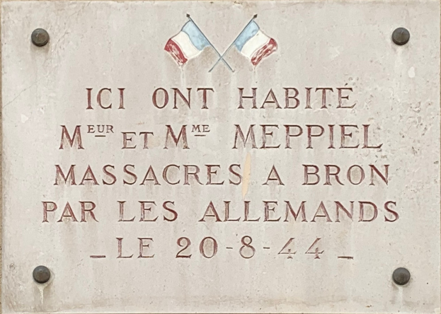 Steintafel an einem Gebäude mit zwei Flaggen darüber, die einen Massaker gedenken.