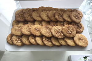 Ein weißer Teller voller Kekse steht auf einem Tisch umgeben von Gläsern und anderen Gegenständen, mit einem Papier unten, das Text und ein Logo anzeigt.