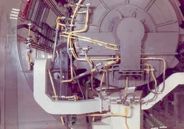 Großes industrielles Accelerator-Gerät mit mehreren verbundenen Komponenten innerhalb eines Gebäudes, das an einer Wand positioniert ist.