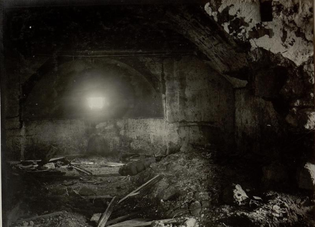 Ein Schwarz-Weiß-Foto eines zerfallenden Tunnels in den Berliner Mauerruinen, mit Schutt auf dem Boden und einem Licht am Ende.