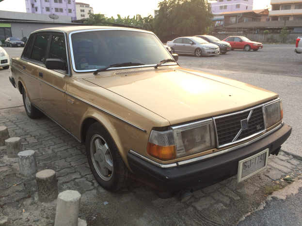 Ein goldfarbenes Auto, das auf der Seite einer Straße mit Gebäuden, Bäumen und einem klaren blauen Himmel im Hintergrund geparkt ist.