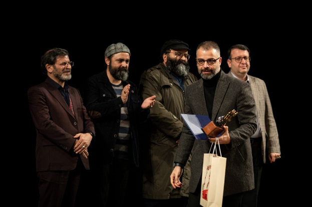 Eine Gruppe von Männern steht auf einer Bühne bei Nacht, einer hölt eine Tasche und eine Trophäe, feiernd die Eröffnung der Berliner Filmfestspiele.