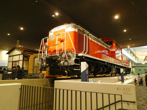 Roter und weißer Zug in einem Museum ausgestellt, umgeben von Besuchern, mit informativen Schildern und strukturellen Elementen.