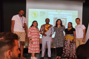 Eine Gruppe von Menschen auf einer Bühne, die lächeln und posen, mit einem Publikum davor und einem Bildschirm im Hintergrund, der 'Open the Knowledge Journalism Awards 2019' anzeigt.