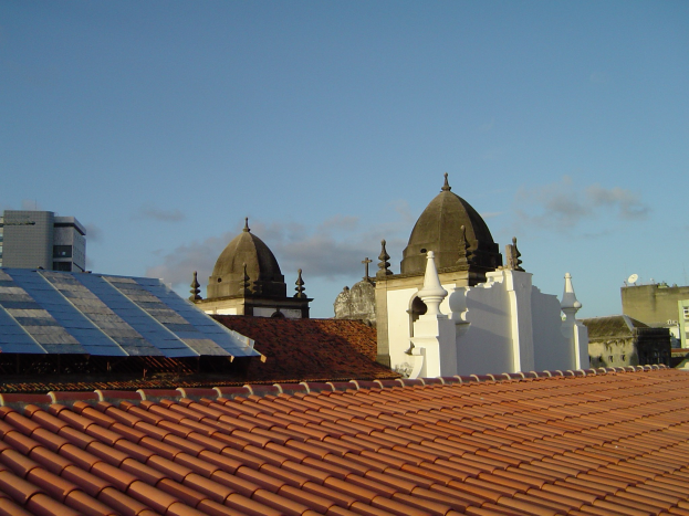 Stadtansicht mit Geb├Ąuden im Vordergrund, Solarpanels auf einem Dach und einem blauen Himmel im Hintergrund.