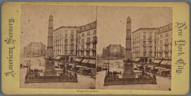 Altes Schwarz-Weiß-Foto einer Stadtstraße mit einem zentralen Denkmal, umgeben von Gebäuden, Straßenmöbeln, Fahrzeugen, Passanten und einem sichtbaren Himmel.