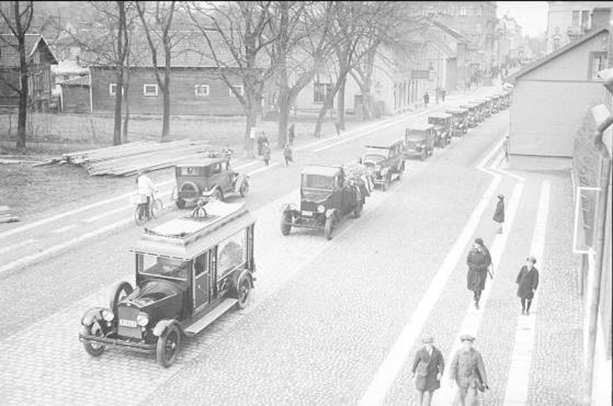 Schwarze und weiße Straßenszene in Berlin aus den 1930er-1940er Jahren, die Autos, Fußgänger, Gebäude mit Fenstern, Bäume und einen klaren Himmel zeigt, mit einem Textüberblatt, das '1930er-1940er Jahre deutsche Autos in Berlin' lautet.
