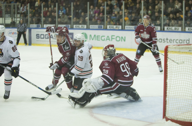 Gruppe von Menschen, die Hockey auf einem Eisstadion spielen, mit Tor auf der rechten Seite, Helmträgern und Stöcken, Zuschauern auf den Tribünen mit Bannern im Hintergrund.