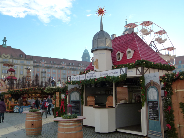 Ein belebter Weihnachtsmarkt in Nürnberg, Deutschland mit Menschen um geschmückte Stände, festlicher Beleuchtung, einem Riesenrad im Hintergrund und einer Tafel mit Text auf der rechten Seite.