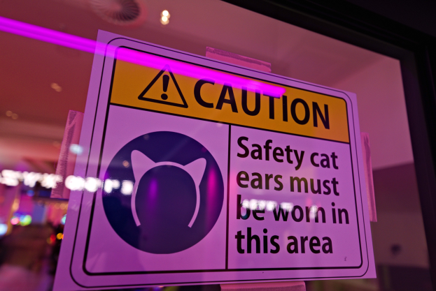 Hellgelbes Warnschild in einem Ladenschaufenster mit der Aufschrift "Vorsicht: Sicherheitskatzenohren müssen in diesem Bereich getragen werden."