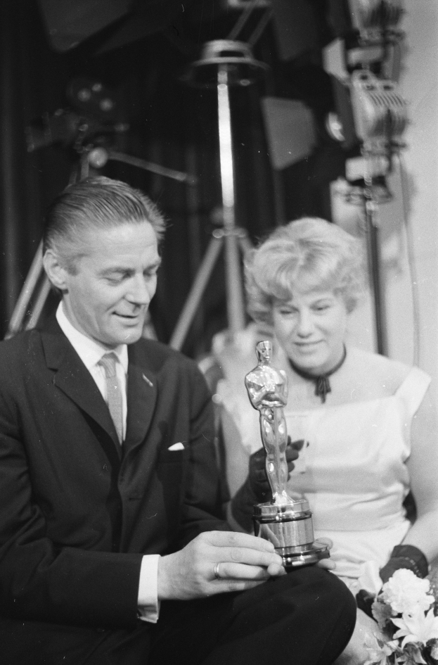 Formal gekleideter Mann und Frau, die zusammen sitzen, Mann hält Oscar-Statue, Frau hält Blumenstrauß, Schwarz-Weiß-Bild.
