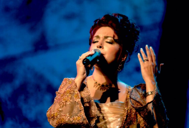 Frau in goldenem Kleid, die auf der Bühne der Eurovision Song Contest in ein Mikrofon singt, mit blau-schwarzem Hintergrund.