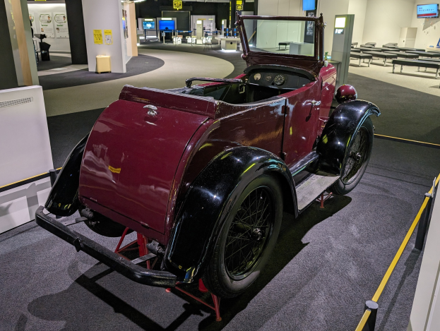 Alter roter Wagen in einem Museum mit Absperrungen, Informationsschildern, Möbeln und Beleuchtung ausgestellt.