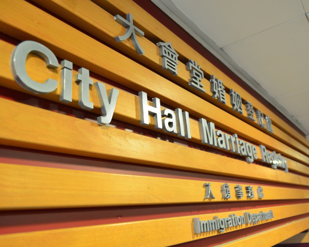 Ein hölzernes Schild an einem Gebäude trägt die Aufschrift "Stadthaus Trauzimmer" mit zusätzlichem Text darunter, unter einer Decke.