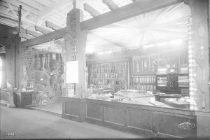 Ein altes Schwarz-Weiß-Foto einer Apotheke mit einem Tresen, auf dem verschiedene Gegenstände und Regale mit Flaschen und anderen Gegenständen im Hintergrund zu sehen sind.