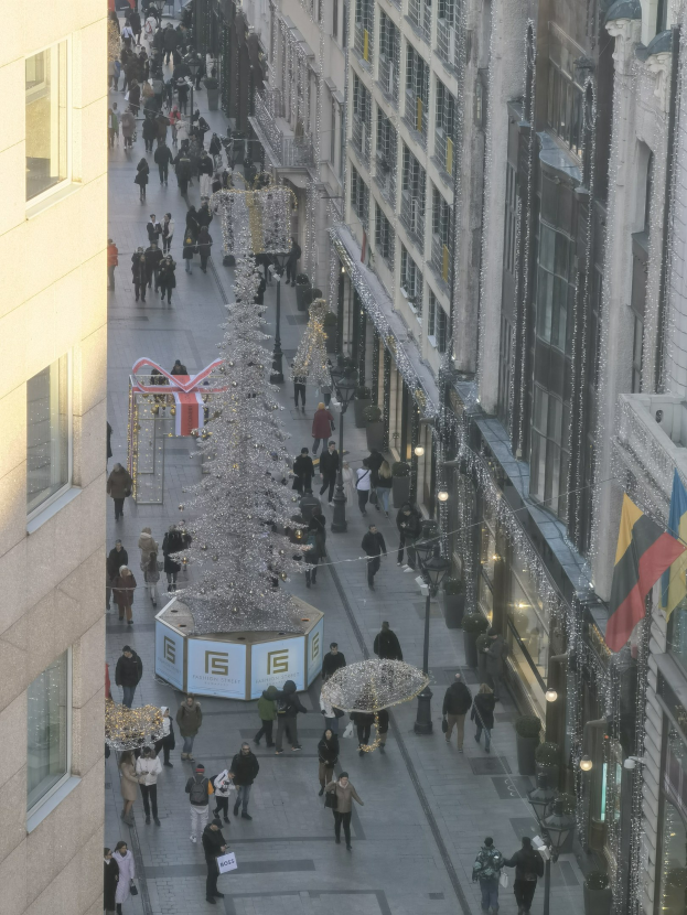 Eine belebte Stadtstraße mit hohen Gebäuden auf beiden Seiten, die einen großen geschmückten Weihnachtsbaum in der Mitte zeigt.