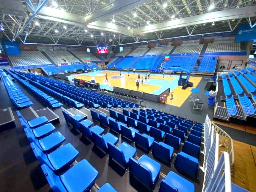 Große Halle in Sarajevo, Bosnien und Herzegowina, mit blauen Sitzplätzen, einem Basketballfeld und Deckenbeleuchtung und -trägern.