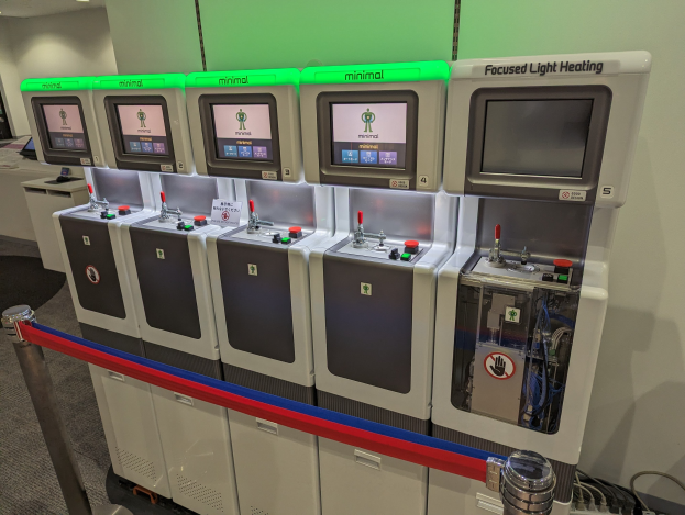 Eine Reihe von Mini-Heizungssystemgeräten mit Steuerknöpfen und -rädchen, die in einem Raum mit einer Wand, Deckenleuchten und einem Boden ausgerichtet sind.