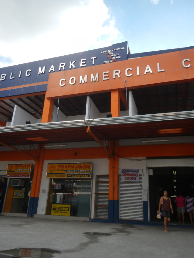 Ein öffentliches Marktgebäude mit Menschen davor, Text auf dem Gebäude und ein sichtbarer Himmel oben.