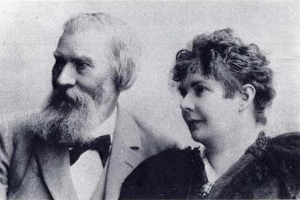 Ein Schwarz-Weiß-Foto von Gustav Klimt und seiner Frau, beide sitzend, mit Klimt im Anzug und seiner Frau, die ihn liebevoll anschaut.