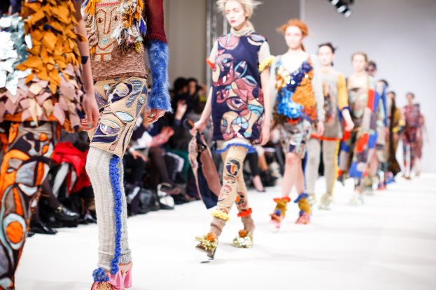 Eine Gruppe Von Frauen Geht Den Laufsteg Bei Der London Fashion Week entlang, Mit Sitzenden Zuschauern Und Heller Beleuchtung Im Hintergrund, Erzeugend Ein Traumhaftes Effekt.