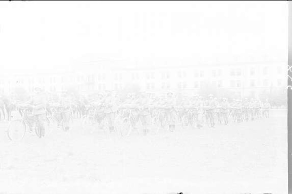 Schwarzes und weißes Foto von Radrennfahrern im Schnee an einem Gebäude vorbei.