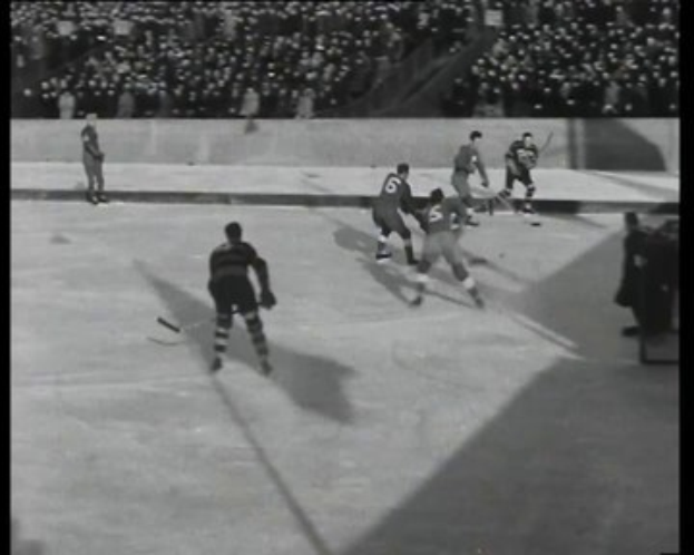 Schwarzes und weißes Foto von Männern, die Hockey auf einem Eisstadion spielen, mit Zuschauern im Hintergrund.