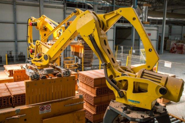 Ein großes Lagerhaus voller Numerous boxes, Kräne und verschiedene Industriegeräte, mit einem Zaun und Pfählen im Vordergrund und einer Wand im Hintergrund.