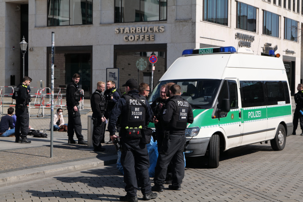 Polizeibeamte vor einem Starbucks-Café mit einem Van auf der rechten Seite und Menschen auf der linken Seite, mit einem Gebäude, einem Schild, einem Laternenpfahl und einer Absperrung im Hintergrund.