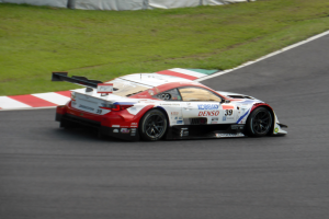 Ein Sportwagen mit Text und Zahlen, der an den 24 Stunden von Le Mans teilnimmt, fährt auf einer Rennstrecke mit Gras an beiden Seiten und einem Zaun im Hintergrund.