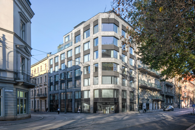 Großes Bürogebäude mit vielen Fenstern, umgeben von Straßeninfrastruktur, Fahrzeugen, Fußgängern, Bäumen und einem bewölkten Himmel, als Sitz eines Unternehmens identifiziert.