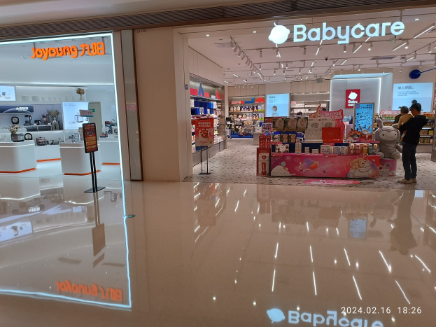Ein Babyladen im Mall of Asia mit Regalen voller Artikel, Schildern, einem Bildschirm, Deckenleuchten und einer Gruppe von Menschen umgeben von Spielzeugen.