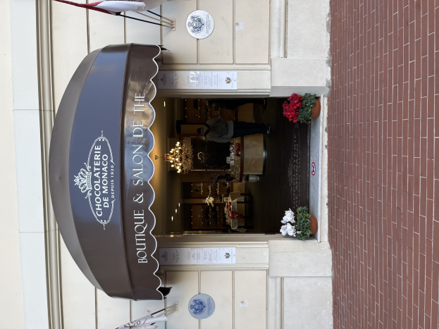 Ein Boutique- und Salon namens 'Boutique & Salon de Monaco' mit Außenbestuhlung, Topfpflanzen und einer beleuchteten Inneneinrichtung.