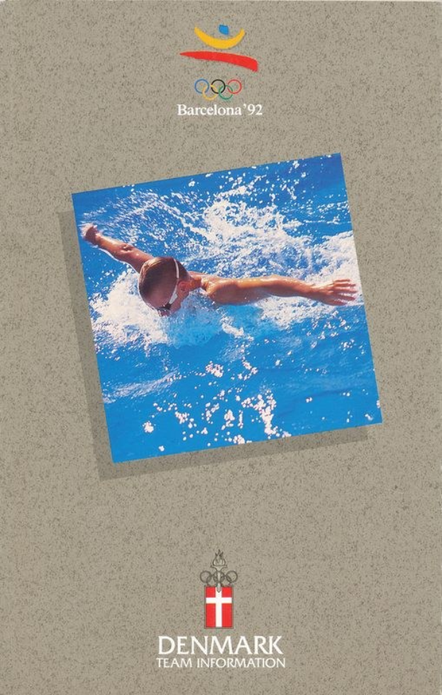 Plakat eines Schwimmers in blauer Badehose mit ausgestreckten Armen im Wasser, unter einem blauen und weißen Olympic Games Barcelona 1992-Logo und "Denmark Team Information"-Text, vor einem hellblauen Himmel mit weißen Wolken.