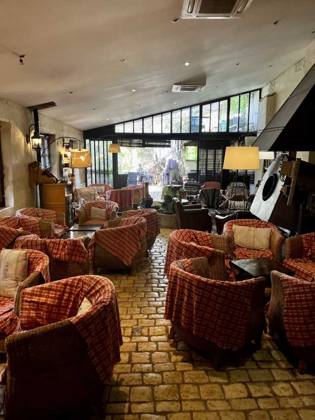 Ein geräumiger Empfangsbereich mit mehreren Stühlen, Tischen, gepolsterten Sofas, wandmontierten Lampen, einer Deckenklimaanlage und Glasfenstern im Hotel de Ville.