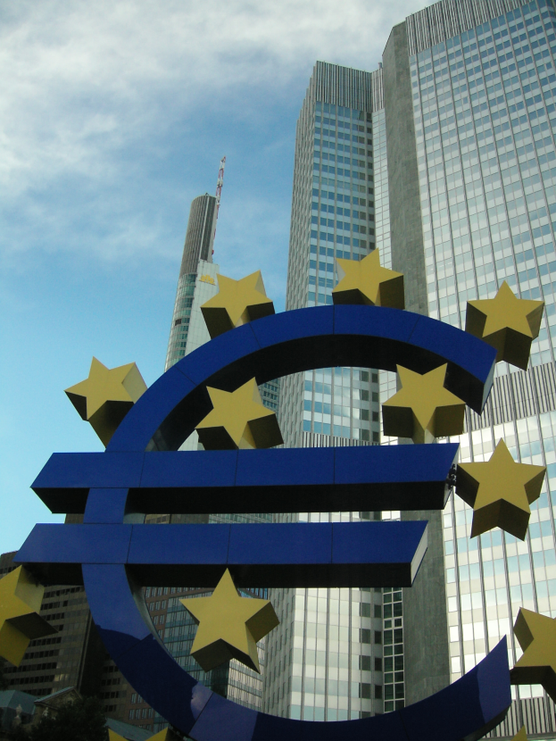 Eurozeichen vor dem Hauptsitz der Europäischen Zentralbank in Frankfurt, Deutschland, umgeben von Bäumen und einem bewölkten Himmel.