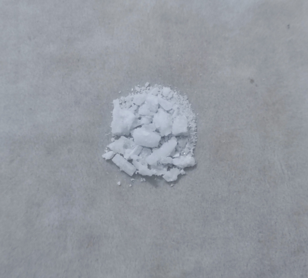 Ein Haufen weißes Salz in der Mitte eines Betonbodens vor einem weißen Hintergrund.