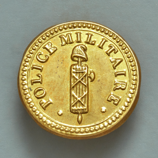 Eine Goldmünze mit der Aufschrift "Police Militaire" vor einem weißen Hintergrund.