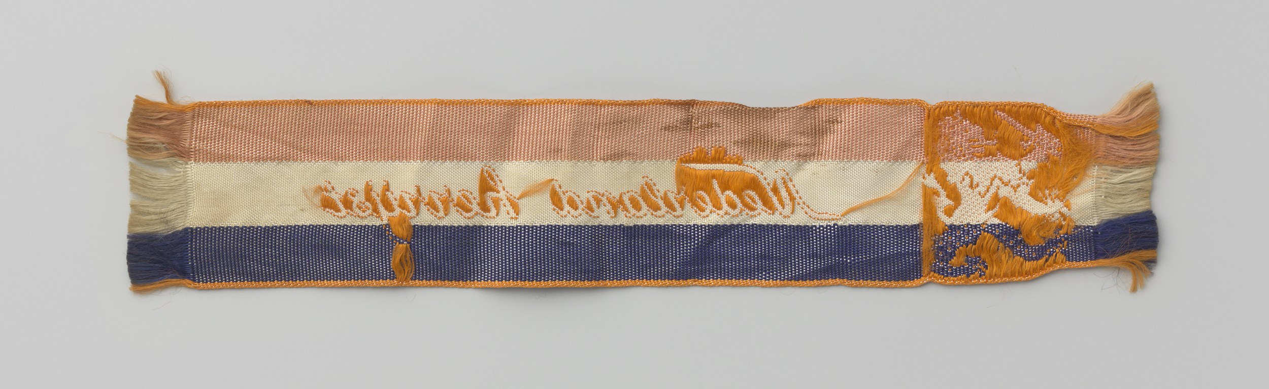 Textilfragment mit einem leuchtenden blau-orangen Streifenmuster und sichtbarem Text.