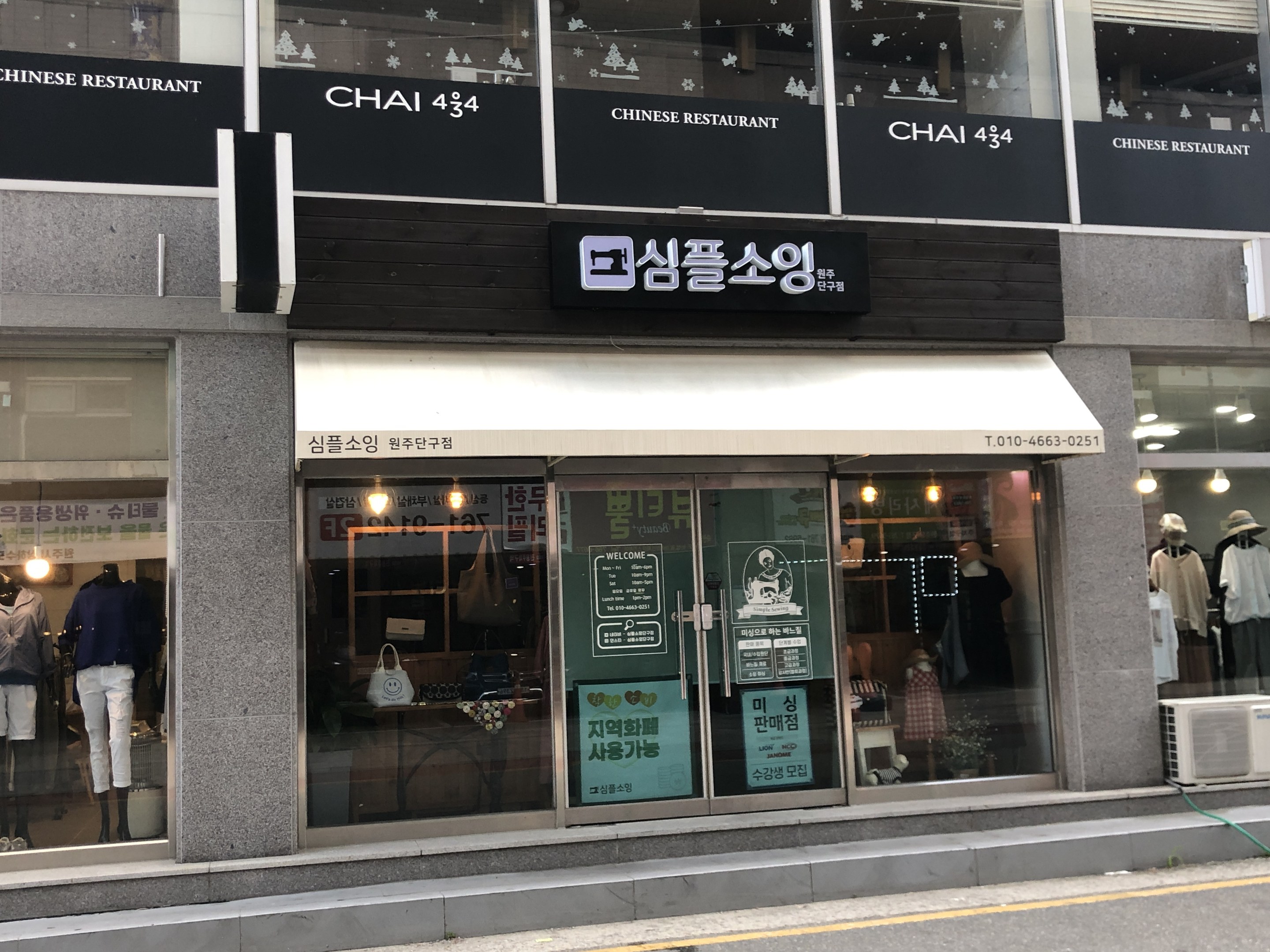 Außenansicht des Chai 434 Chinesischen Restaurants in Seoul, Südkorea, mit Glaswänden, Schaufensterpuppen in Kleidern, beleuchteten Tafeln, einer Klimaanlage auf der rechten Seite und einer Straße unten.
