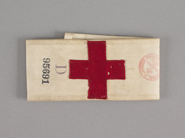 Ein rotes Kreuz-Ersthelfer-Set in einer Stofftasche mit Text und einem Stempel, das auf einer Oberfläche liegt.