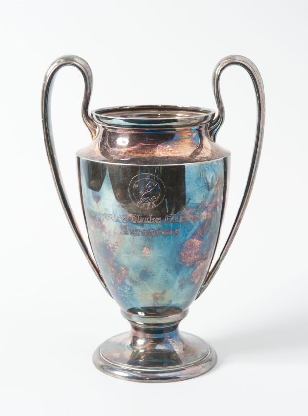 Der UEFA-Champions-League-Pokal, ein stählerner Becher mit zwei Griffen, blau und silbern in der Farbe, mit der Aufschrift «UEFA Champions League», vor einem weißen Hintergrund dargestellt.