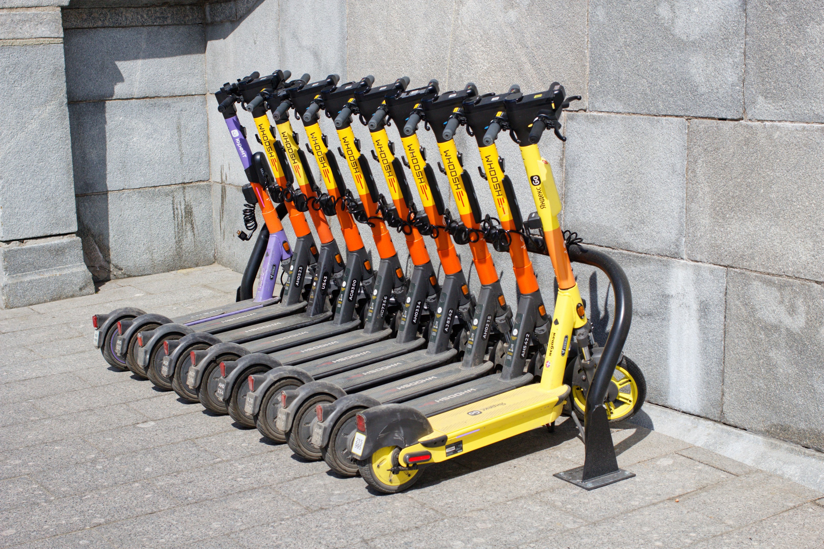 Eine Reihe von Elektro-Scootern ordentlich auf einem Gehweg geparkt mit einer Wand im Hintergrund.