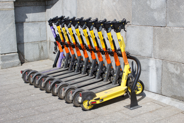 Eine Reihe von Elektro-Scootern ordentlich auf einem Gehweg geparkt mit einer Wand im Hintergrund.