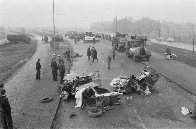 Schwarz-weiß-Szene eines Autounfalls am Straßenrand mit mehreren Fahrzeugen und einer Gruppe von Menschen in der Nähe, Laternenpfähle, Bäume und Himmel im Hintergrund.