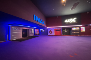 Innenansicht eines Kinos mit lila Teppich, text- und bildschirmgeschmückten Wänden und Deckenbeleuchtung.