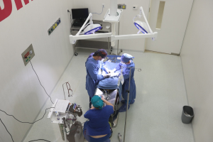 Chirurgen führen eine Operation an einem Patienten auf einer Trage in einem Operationssaal mit medizinischer Ausrüstung und einem Monitor im Hintergrund durch.